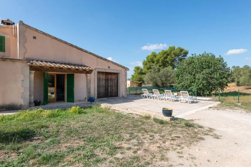 Una casa da a un patio pavimentado con asientos al aire libre y árboles.