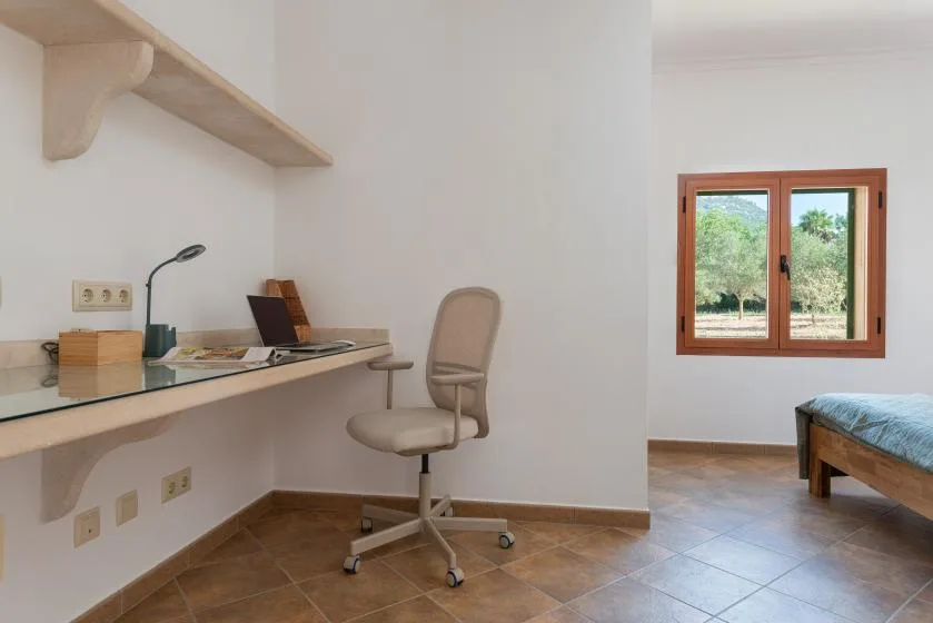 Un escritorio con una silla está junto a un dormitorio con ventana.