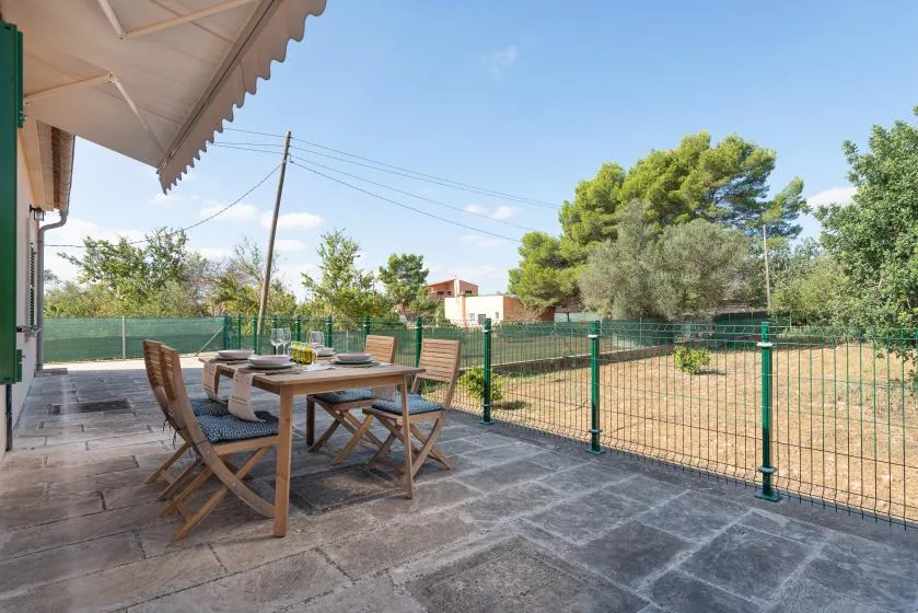 Un patio exterior con una mesa de comedor y asientos junto a un jardín cercado.