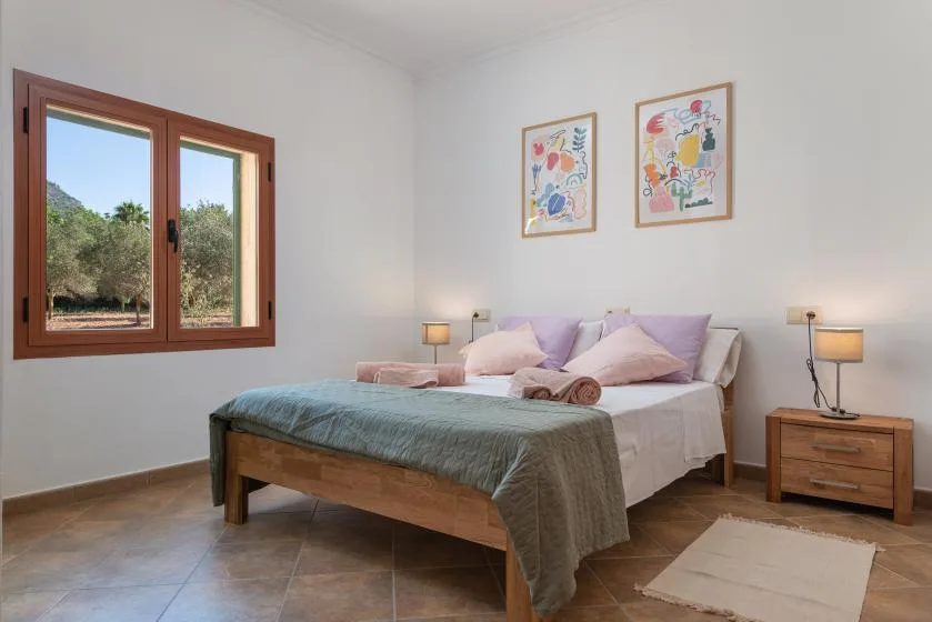 Un dormitorio con una cama bien tendida debajo de dos cuadros enmarcados.