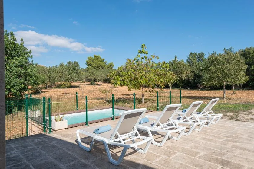 Una piscina con tumbonas en un patio pavimentado junto a una zona arbolada.
