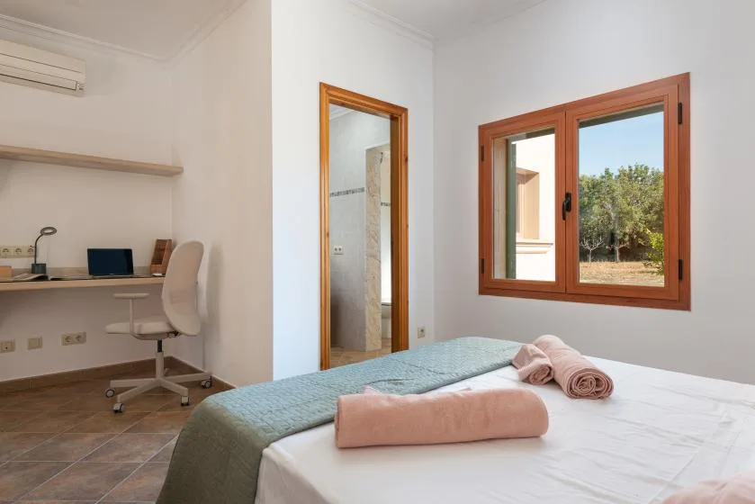Un dormitorio con una cama junto a un escritorio y una ventana con vistas a la vegetación.