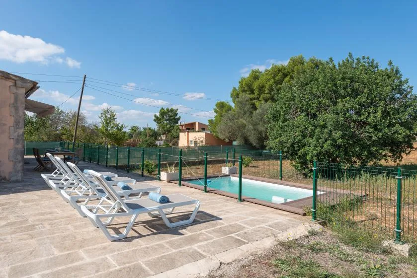 Una piscina al aire libre está junto a un patio pavimentado con asientos reclinables.