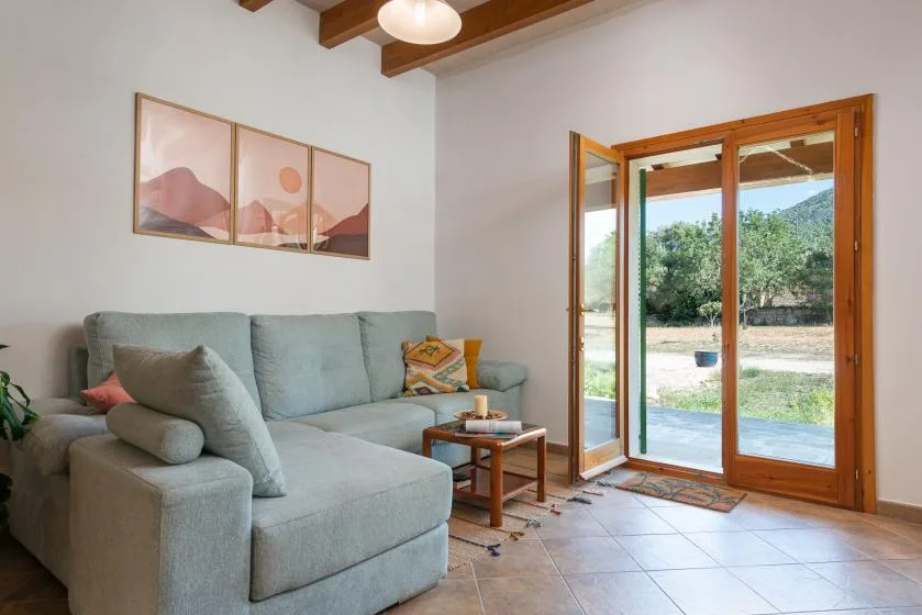 Una sala de estar con asientos junto a puertas de vidrio abiertas y vegetación al fondo.