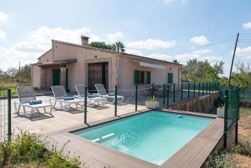 Una pequeña piscina exterior junto a una casa, con asientos en el patio pavimentado.