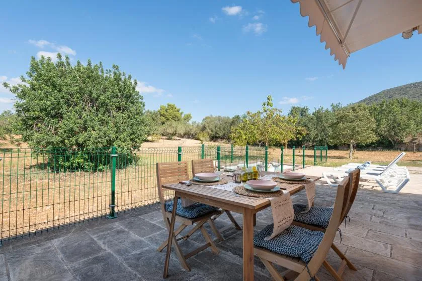 Una zona de comedor al aire libre con mesa y sillas de madera da a un paisaje arbolado y cercado.