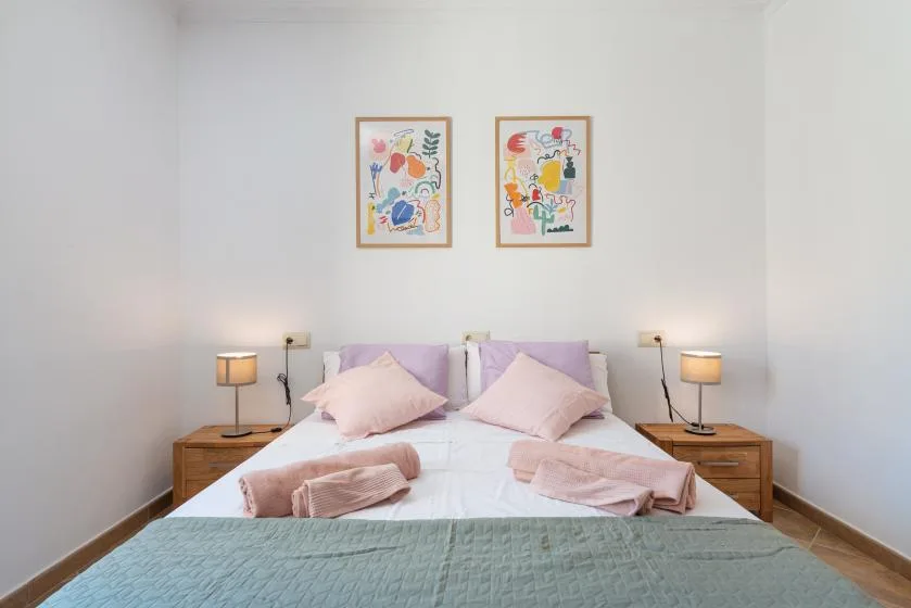 Un dormitorio con una cama doble, mesitas de noche y cuadros coloridos sobre el cabecero.