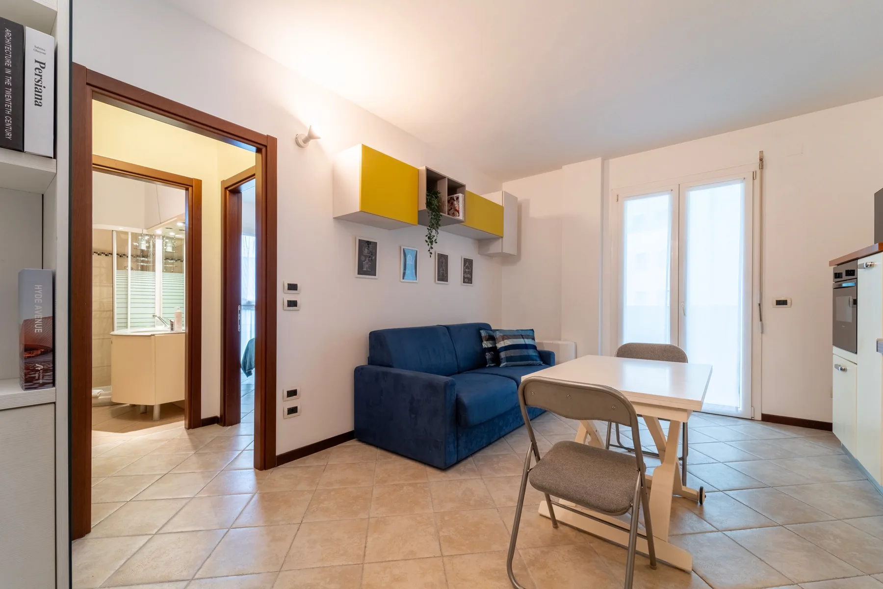 A bright living and dining area with a blue sofa, table, and balcony doors.