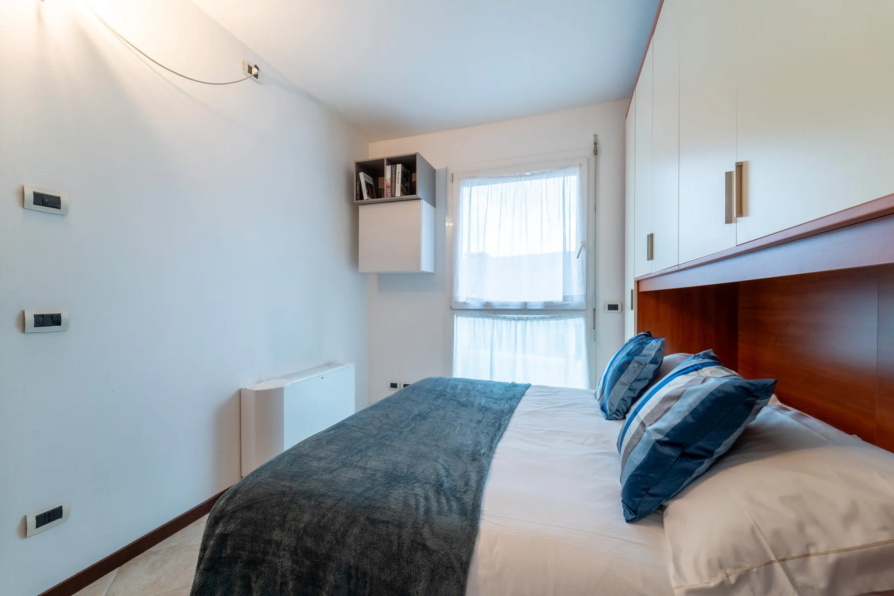 A bedroom with a bed and a window covered by sheer curtains.