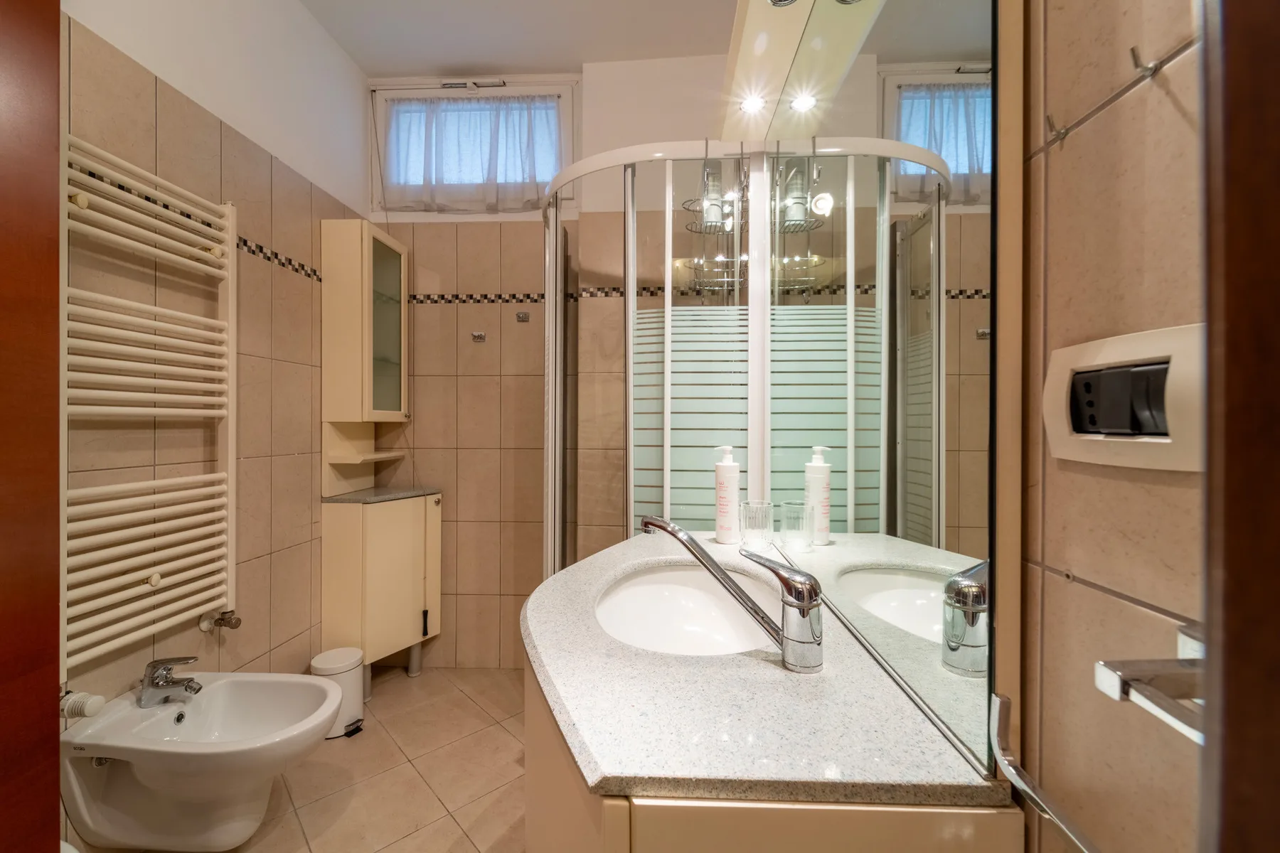 A tiled bathroom with a curved glass shower and a sink vanity.