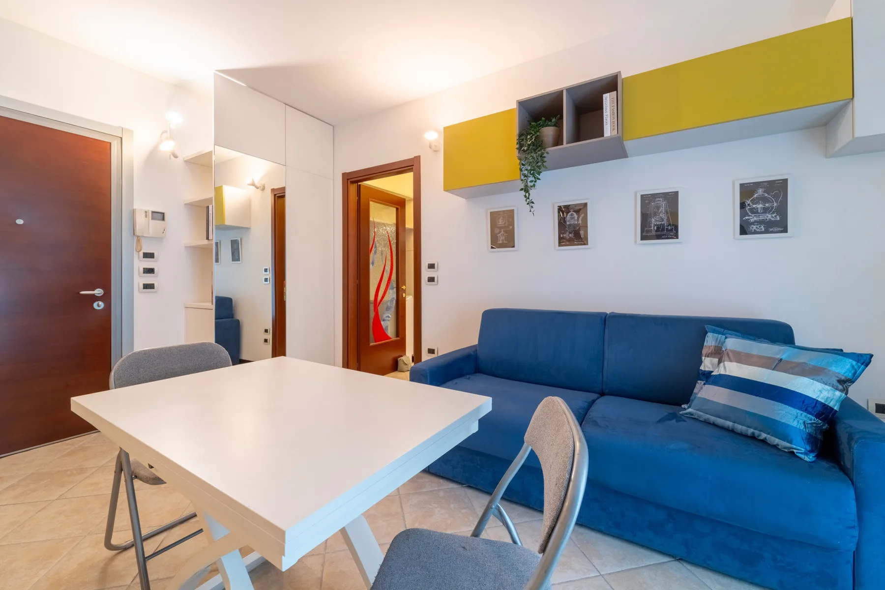 A living room with blue seating, a white table, and wall-mounted cabinets.