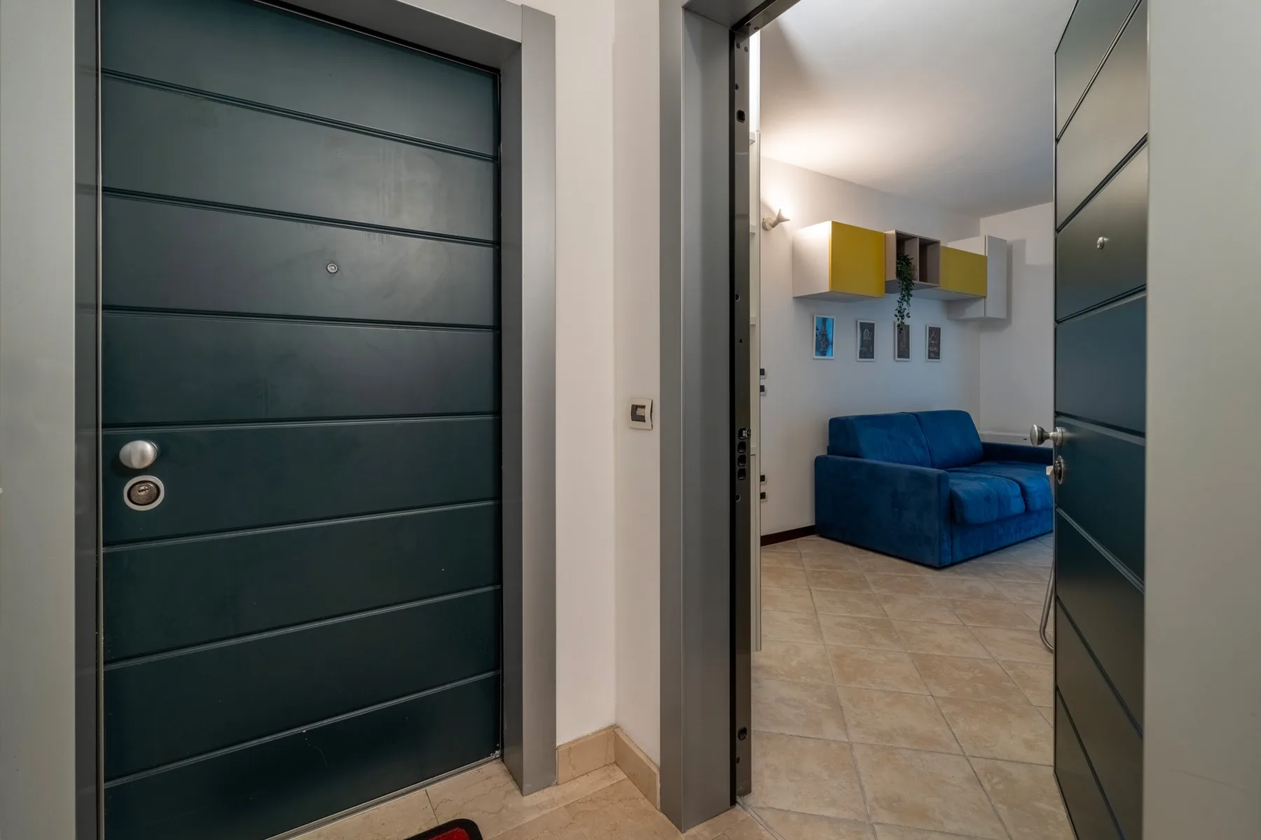 A tiled entryway opens onto a living area with blue seating and wall-mounted cabinets.