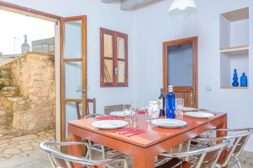 Un comedor con la mesa puesta y una puerta abierta junto a un muro de piedra.
