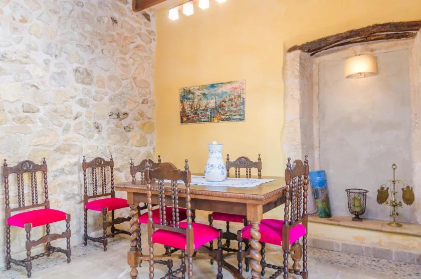 Comedor con una mesa de madera, asientos tapizados de colores vivos y paredes de piedra.