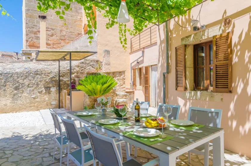 Un comedor al aire libre con una mesa larga y sillas bajo enredaderas frondosas.