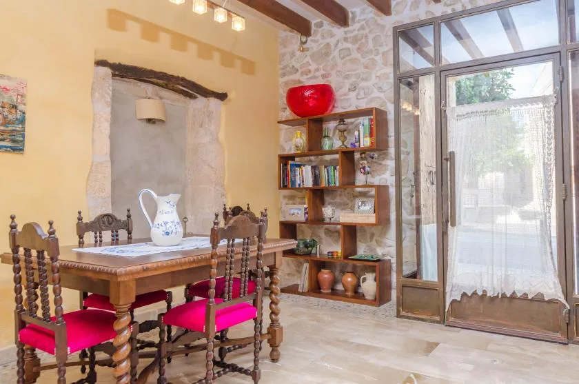 Un comedor con una mesa de madera, sillas con cojines rojos y una puerta de vidrio.