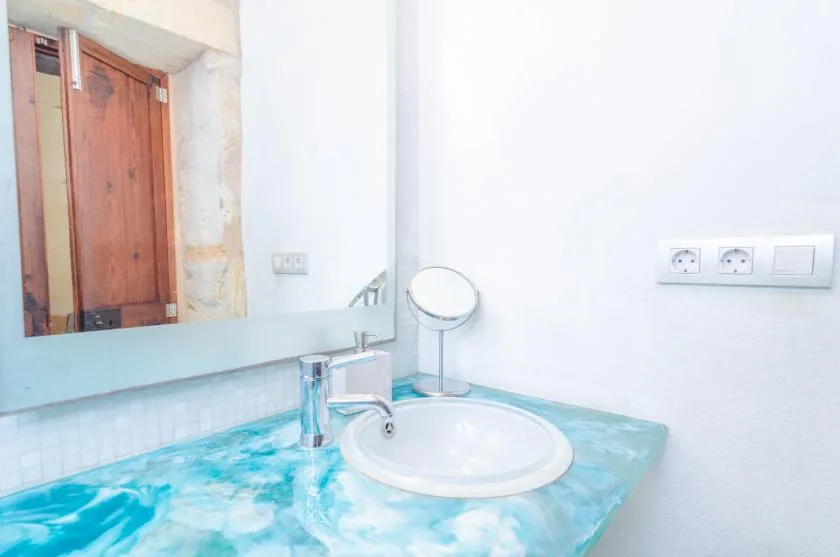 Un lavabo de baño con un lavamanos blanco, espejo y encimera turquesa.