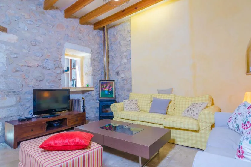 Una sala de estar con un sofá amarillo, un televisor y una mesa de centro baja.