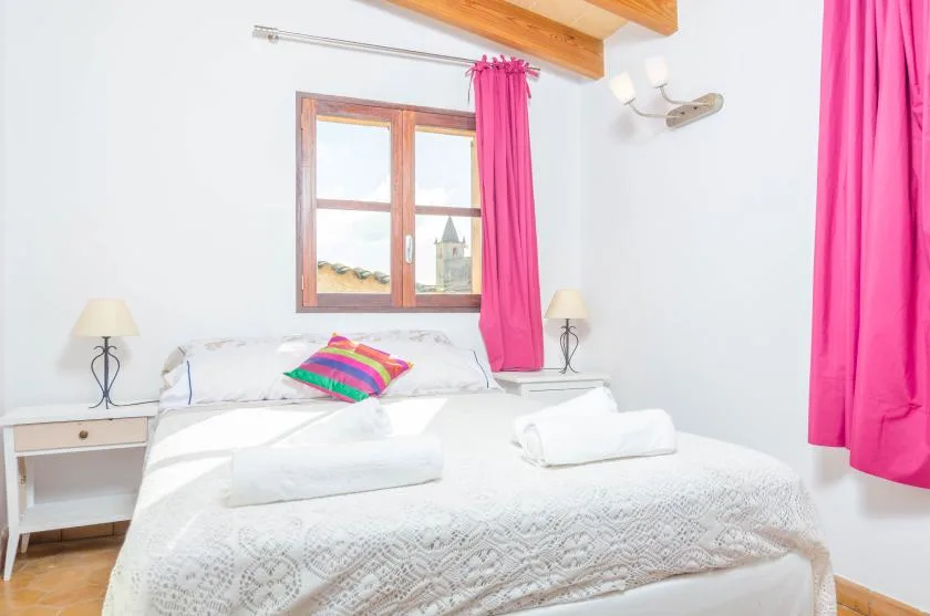 Un dormitorio con una cama bajo una ventana enmarcada por cortinas rosas.