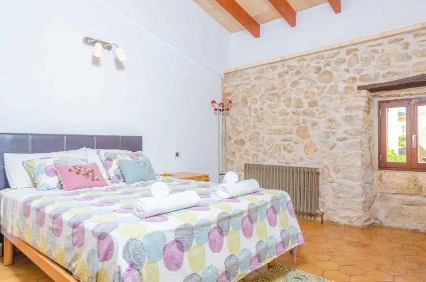 Un dormitorio con una colcha estampada de colores, vigas vistas y una pared de piedra.