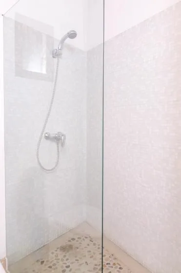 Zona de ducha con azulejos, ducha de mano y suelo con patrón de guijarros.
