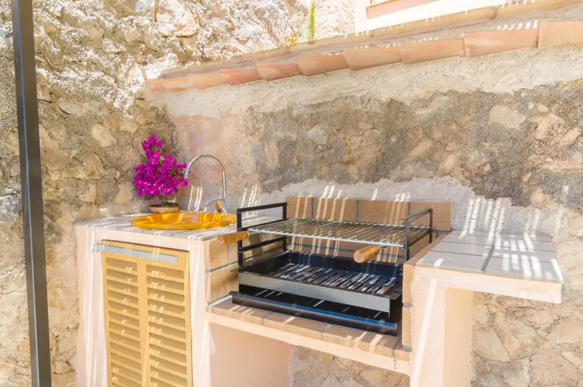 Una zona de cocina al aire libre con parrilla y fregadero junto a un muro de piedra.