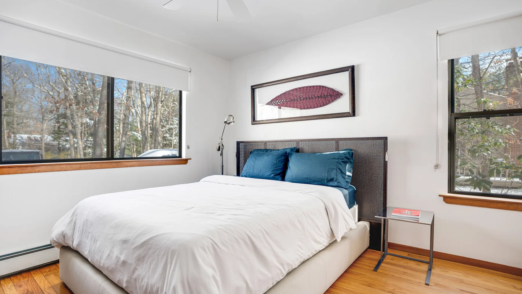 A bedroom with a bed, blue pillows, and large windows overlooking trees.