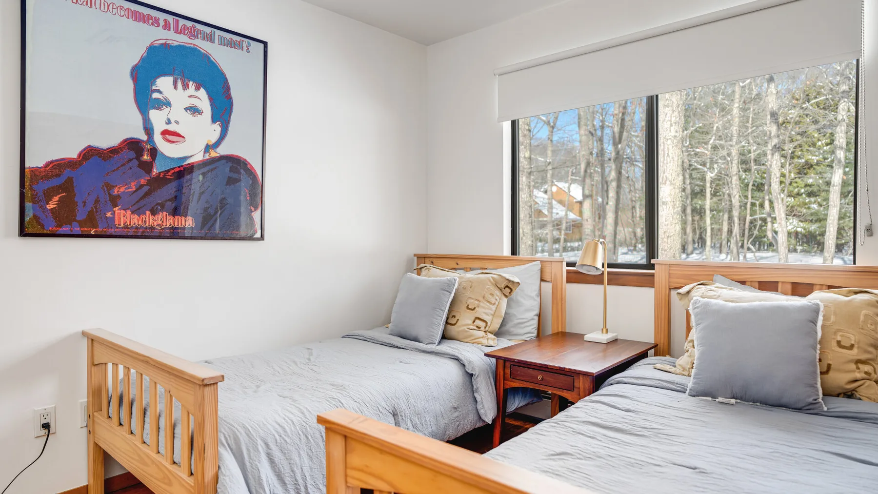 A bedroom with two beds beneath a large window overlooking trees.