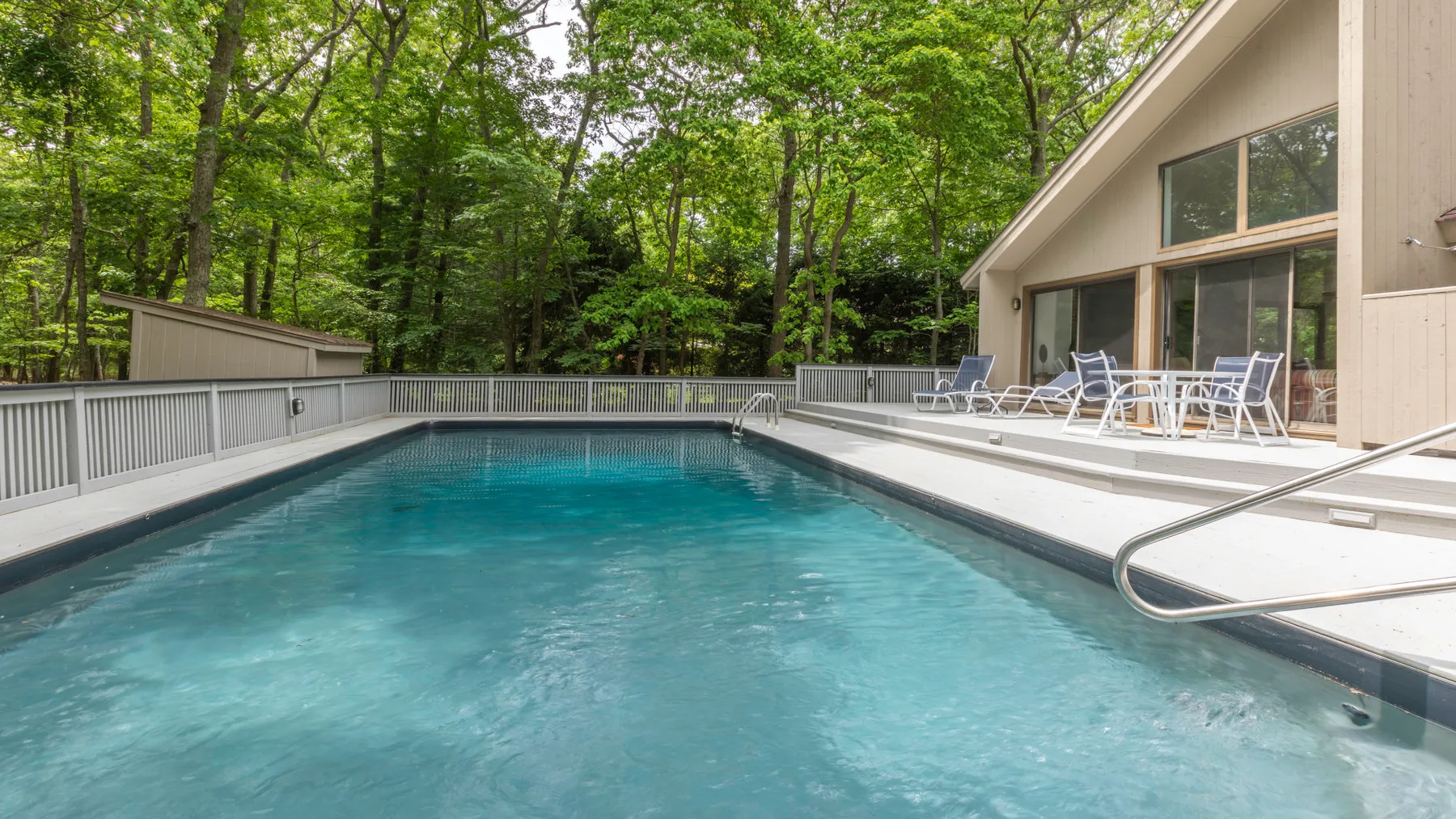 An outdoor swimming pool beside a building, surrounded by trees.
