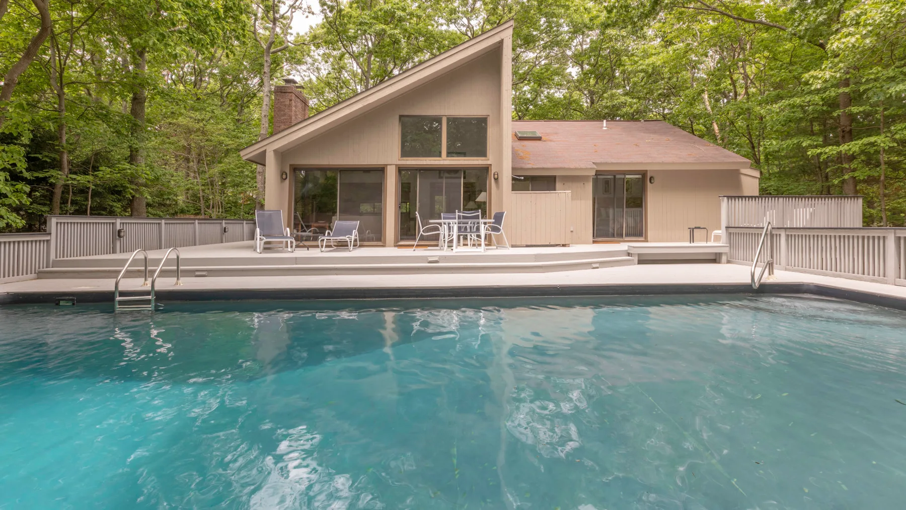 A swimming pool in front of a modern house surrounded by trees.