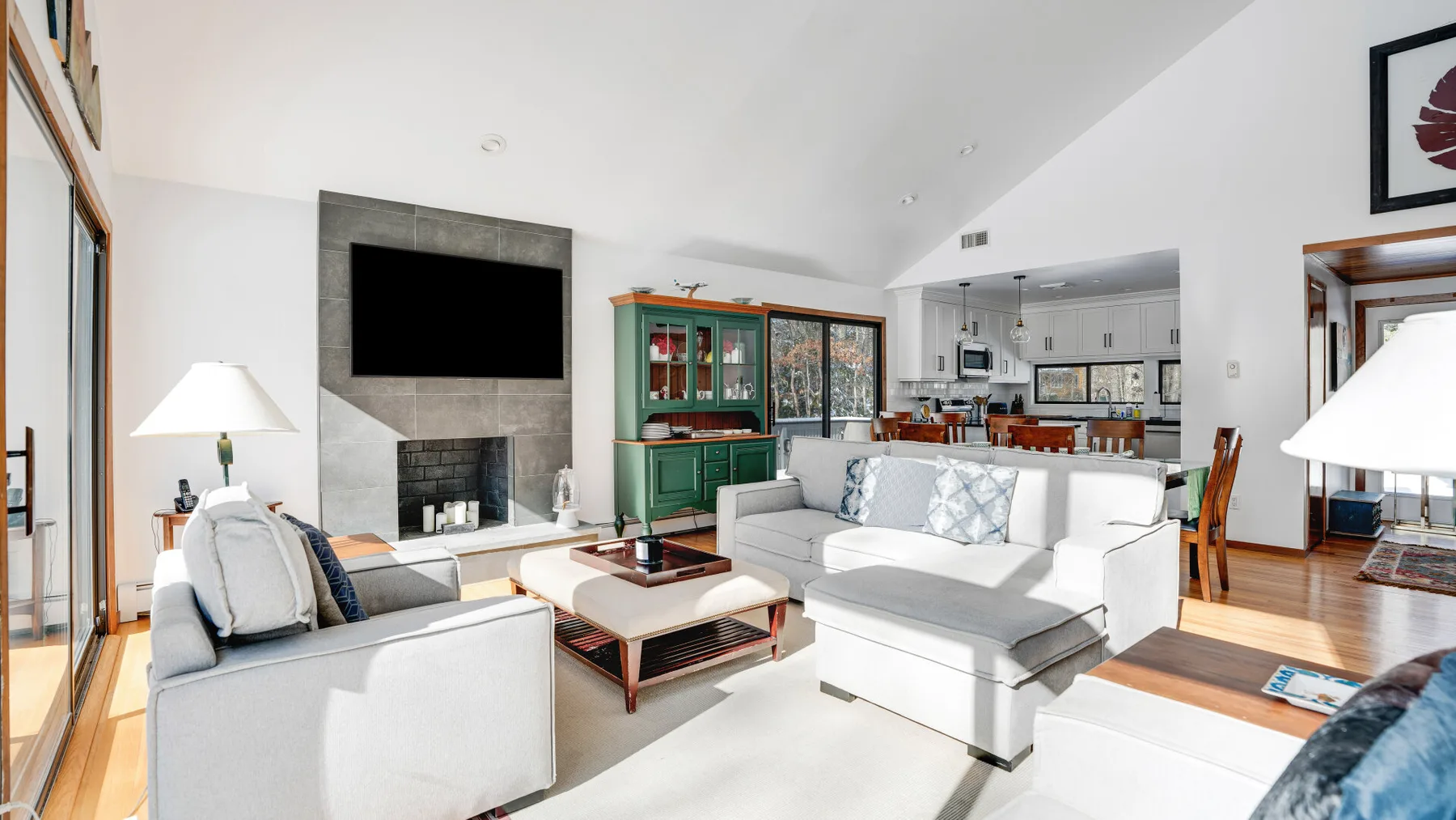 A bright living room with white seating, a coffee table, and a large television.