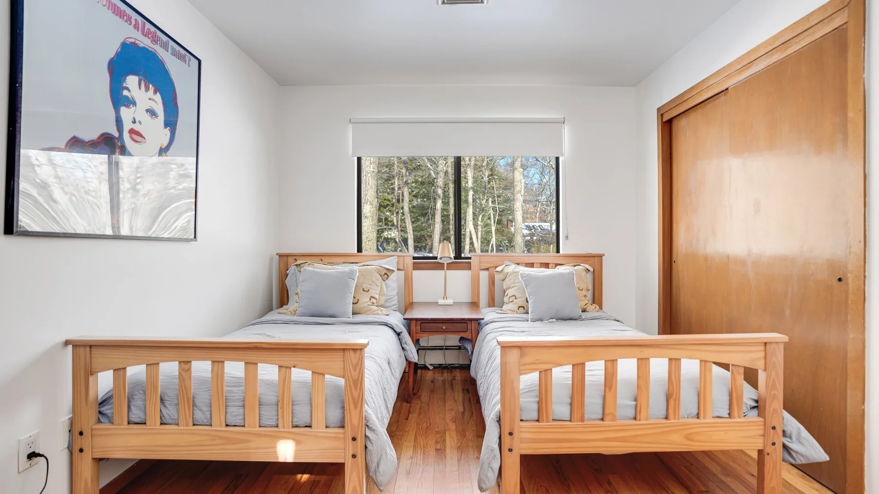 A bright bedroom with two wooden beds and a window overlooking trees.