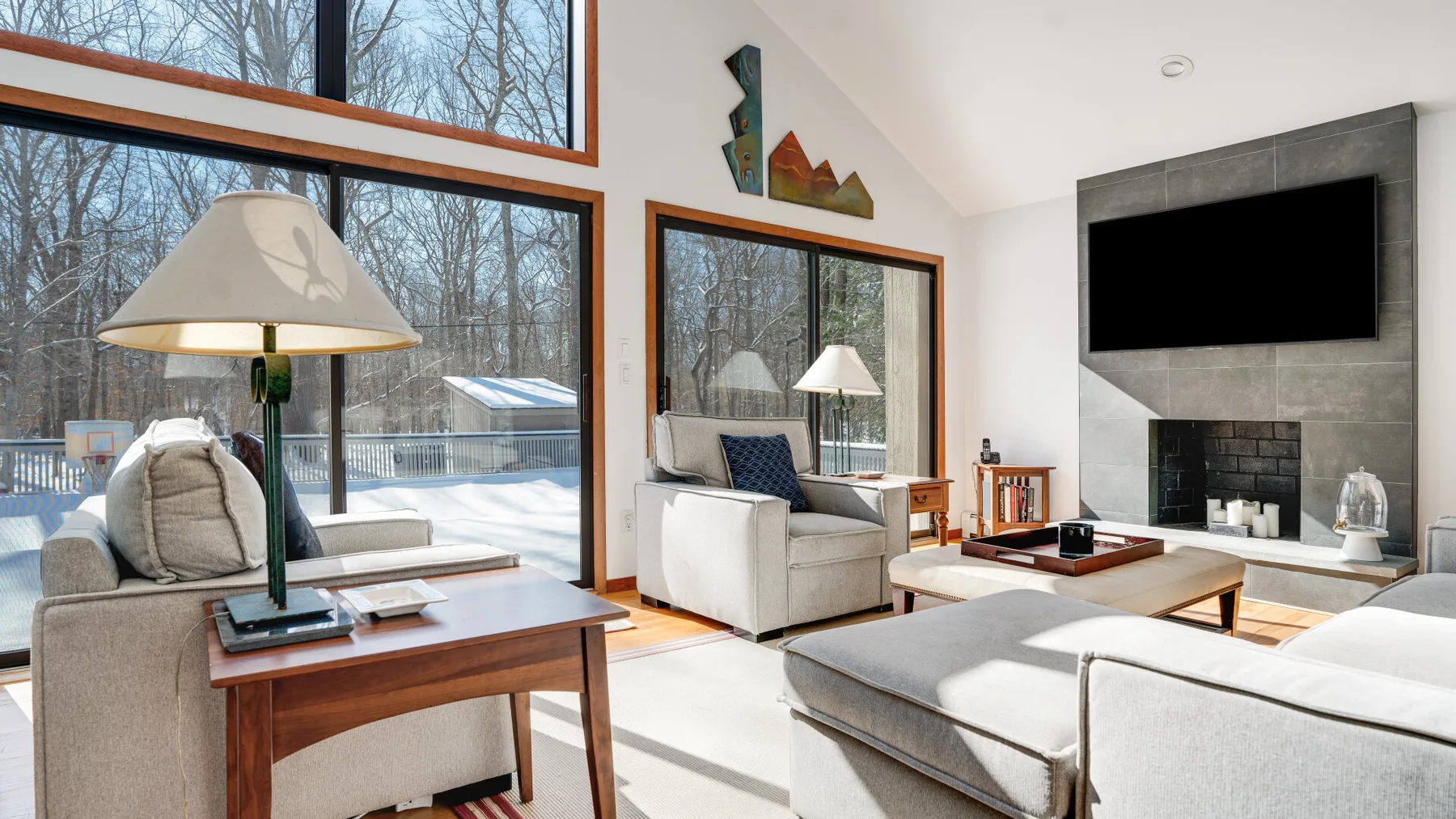 A bright living room with large windows, seating, and a wall-mounted television.