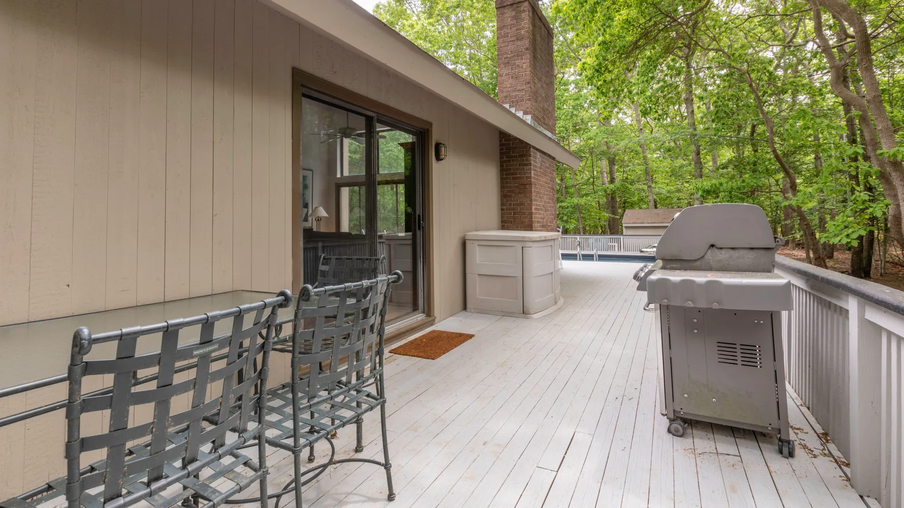 An outdoor deck with seating and a grill, surrounded by trees.