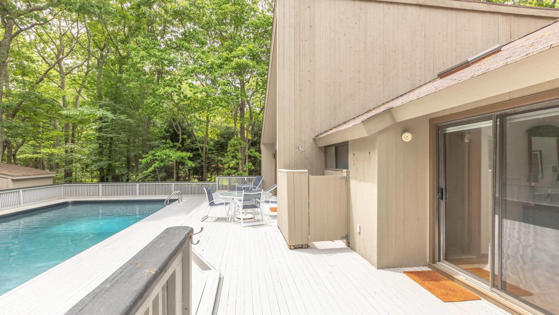 A poolside deck beside a building, with outdoor seating and trees in the background.