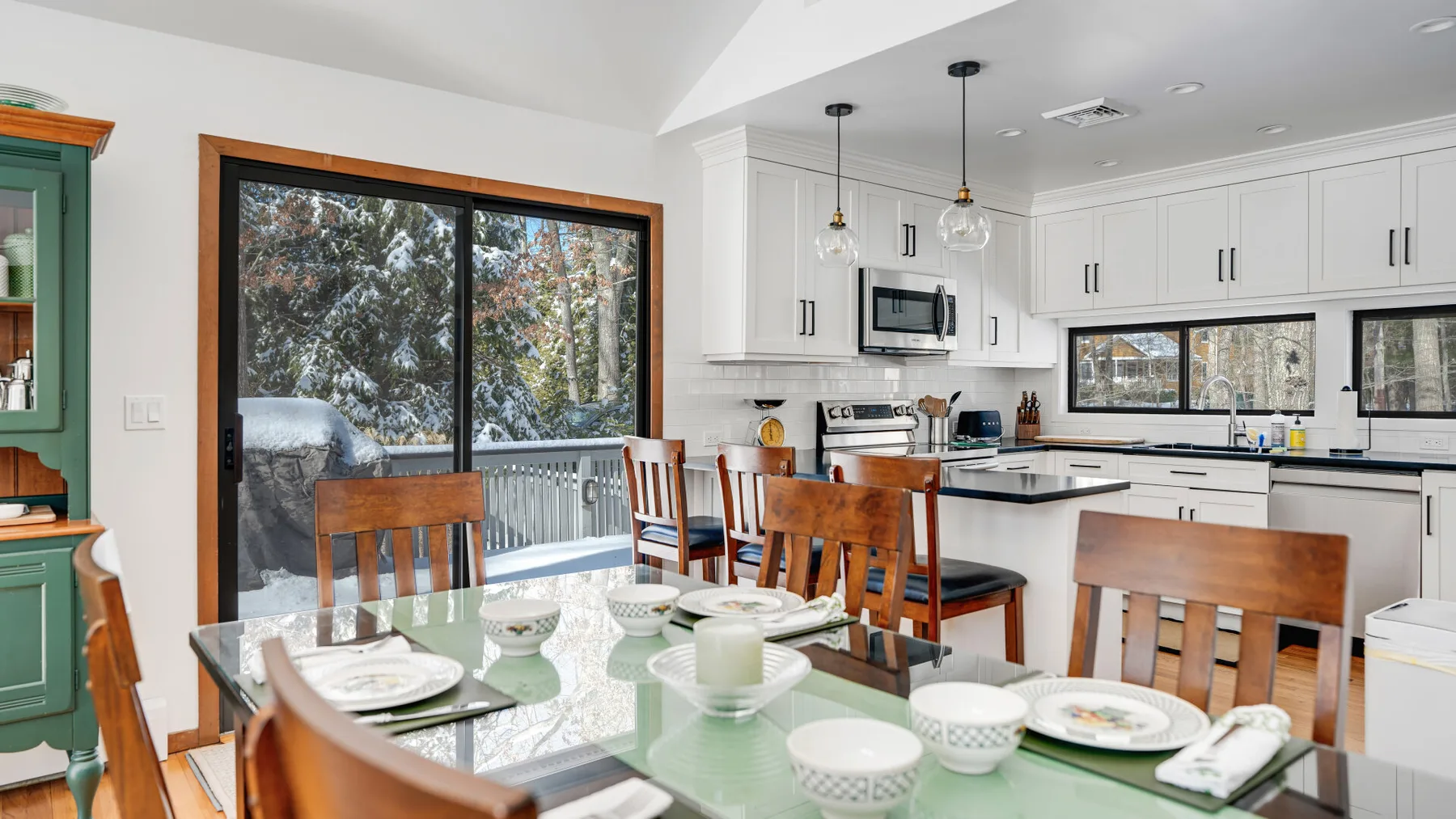 A dining area opens into a bright kitchen, with a glass table beside the windows.