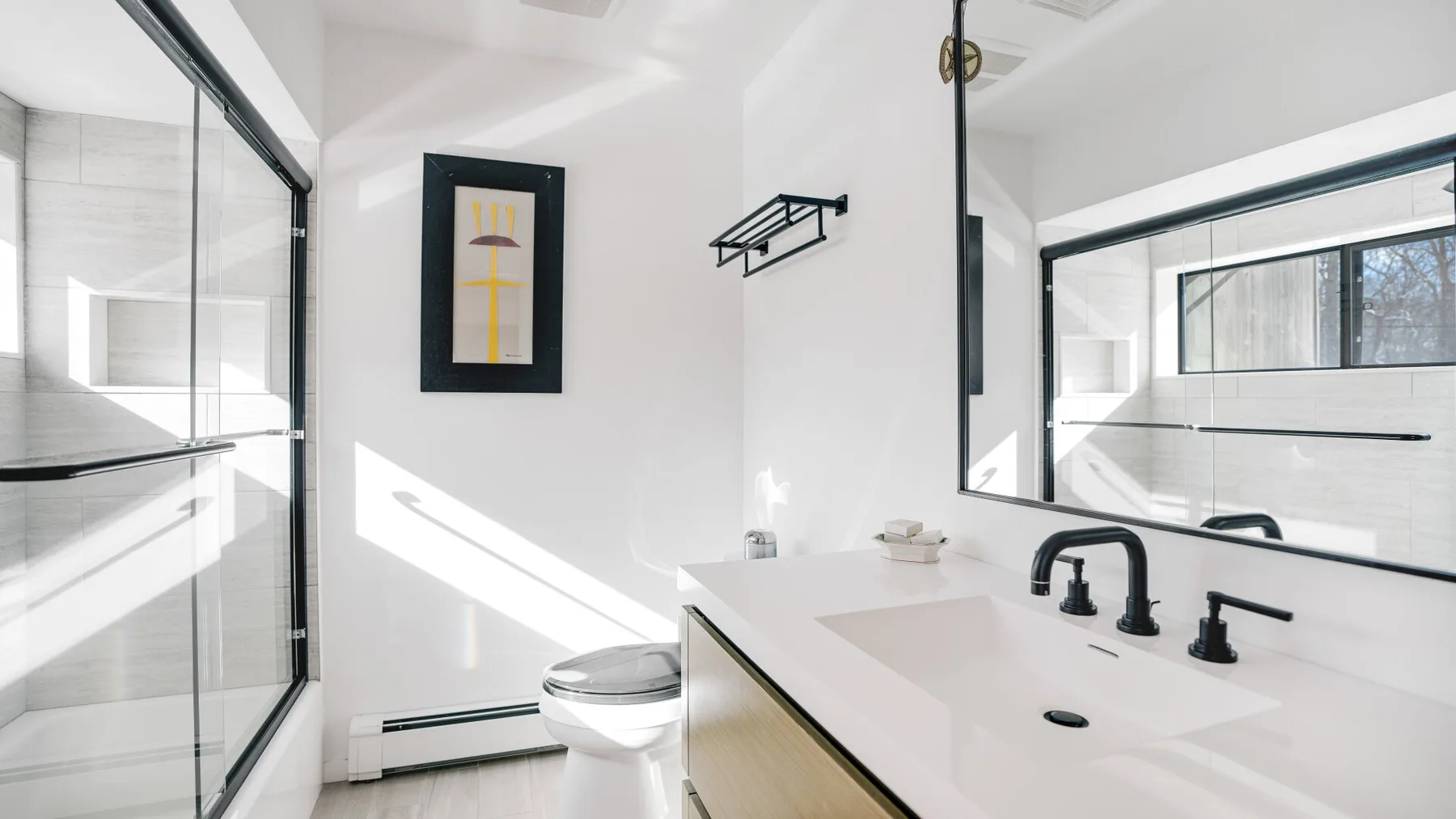 A bright bathroom with a glass shower, toilet, and long vanity.