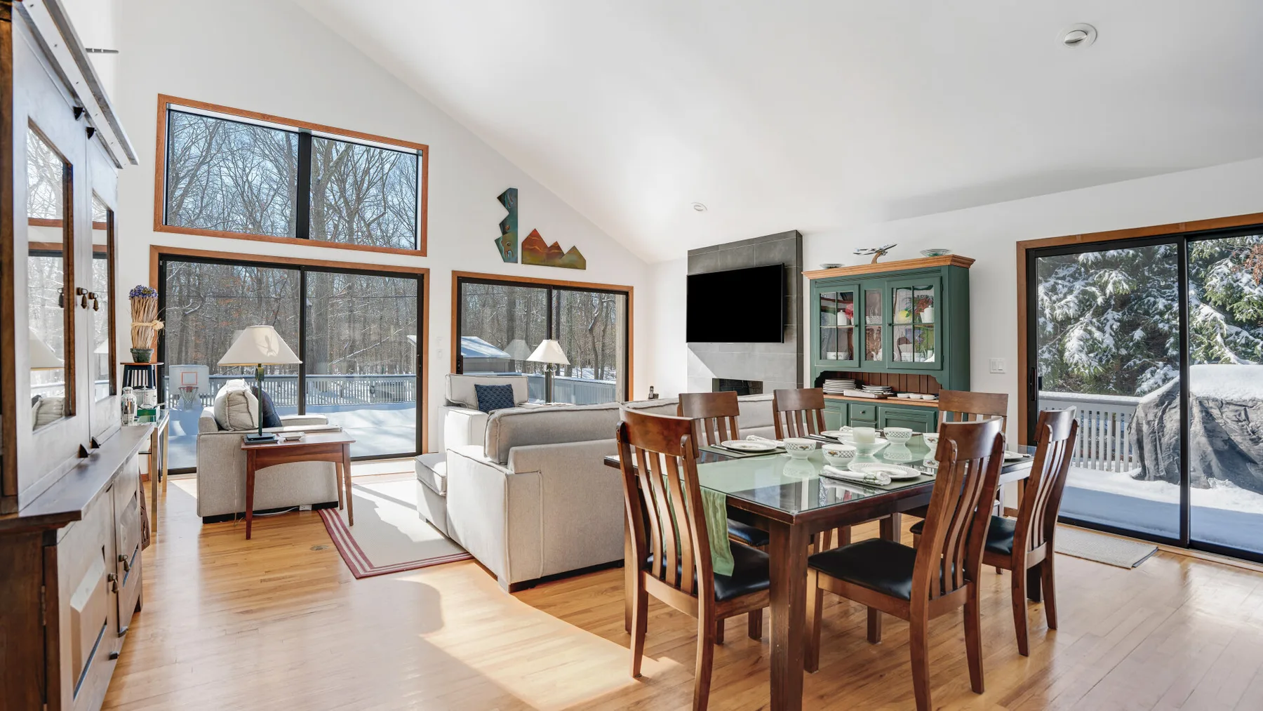 A bright living and dining area has large windows and a wooden dining table.