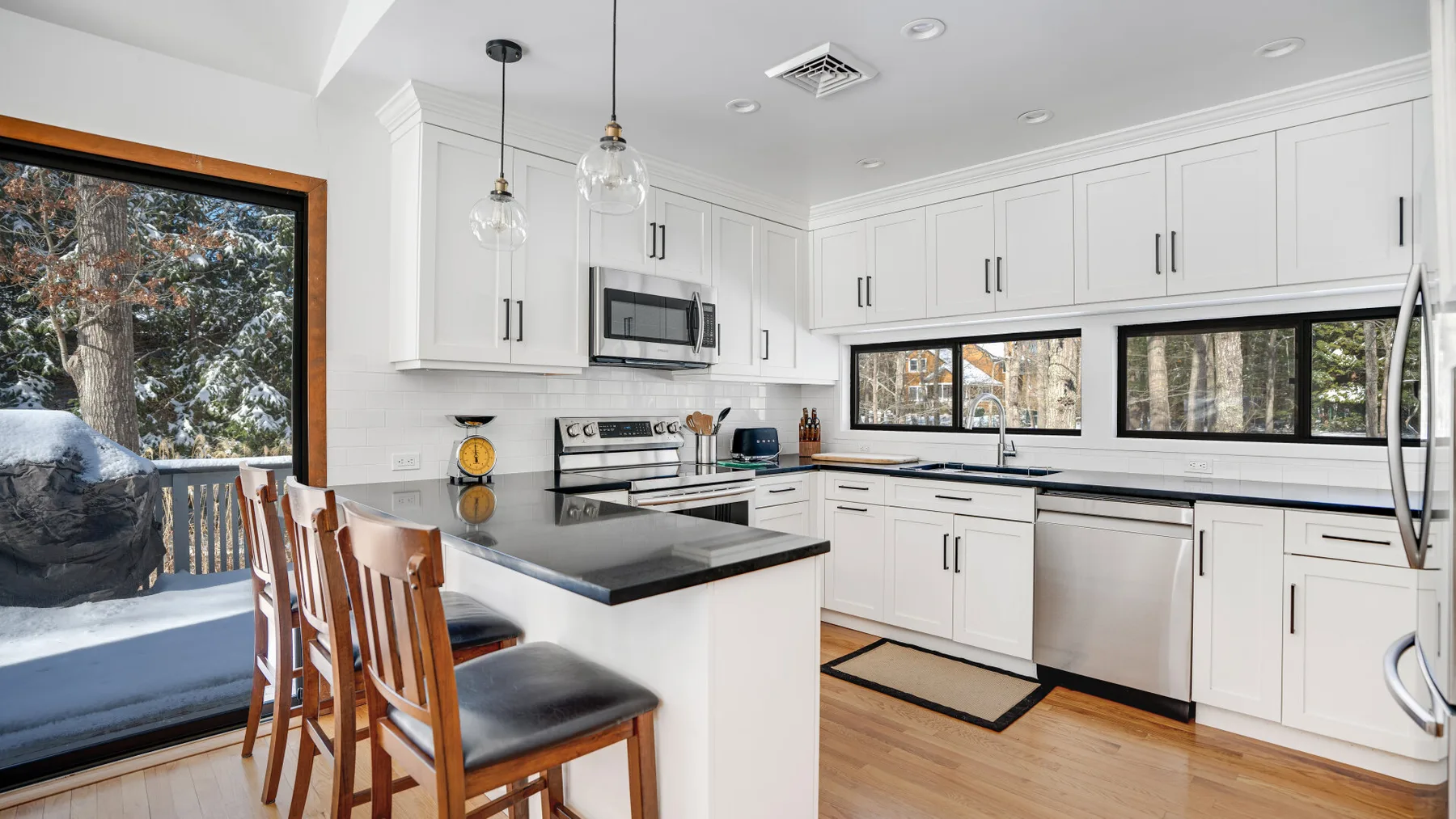 A bright kitchen with white cabinets, a central island, and windows overlooking trees.