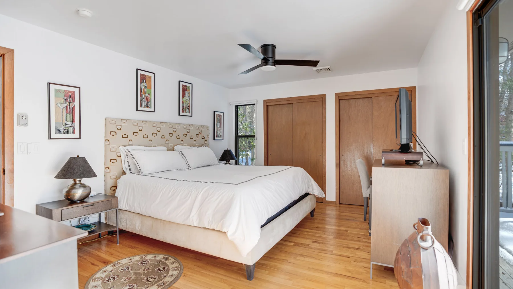 A bright bedroom with a neatly made bed and framed artwork on the walls.
