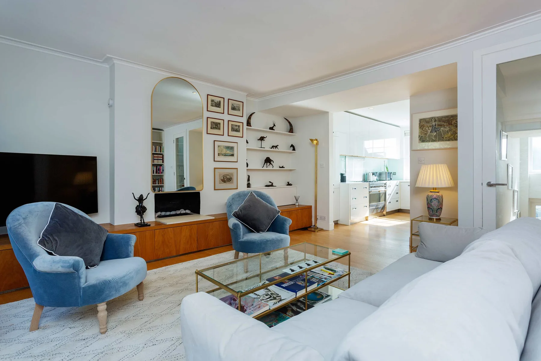 A bright living room with blue seating, a television, and a glass coffee table.