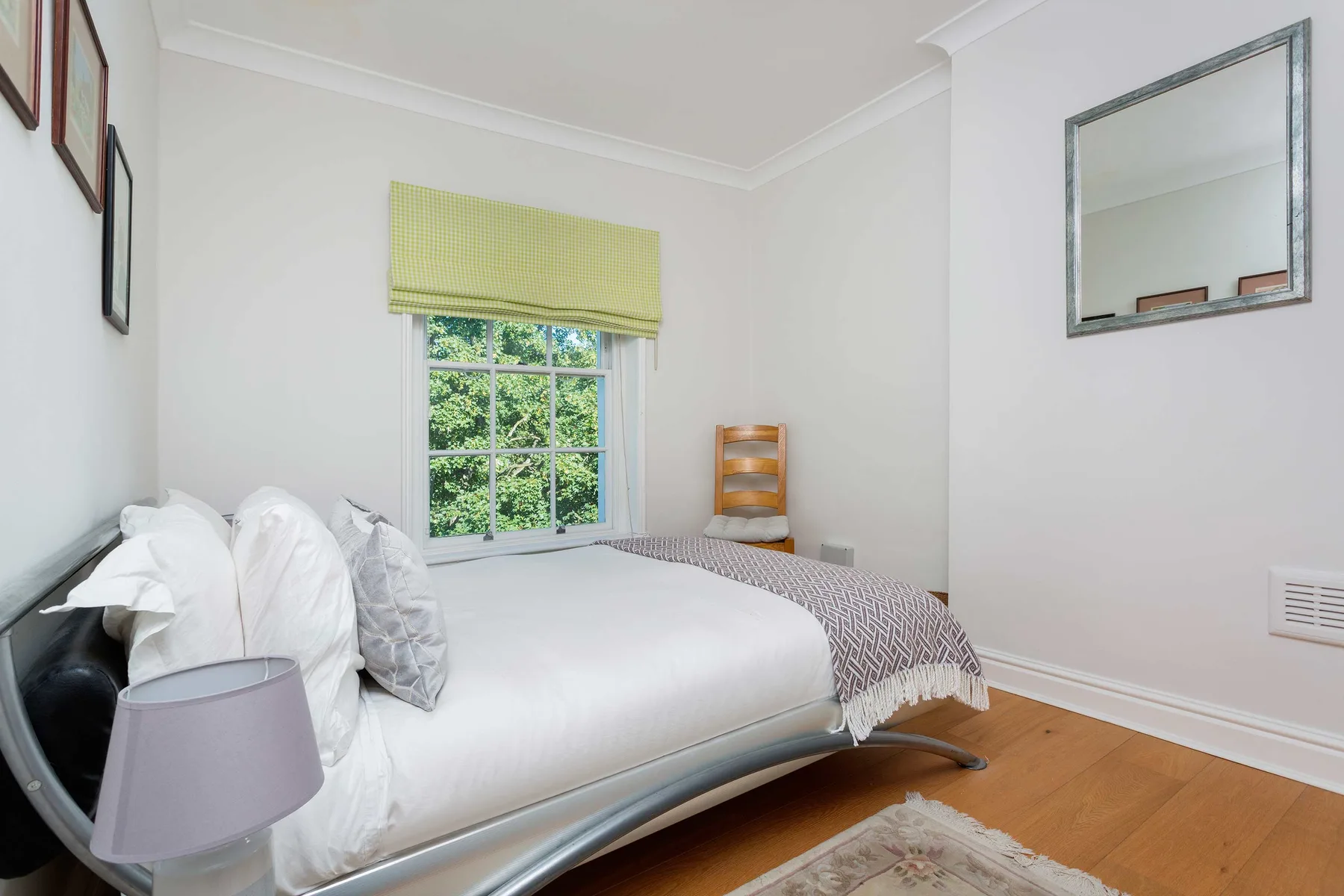 A bedroom with a bed beneath a window overlooking leafy greenery.