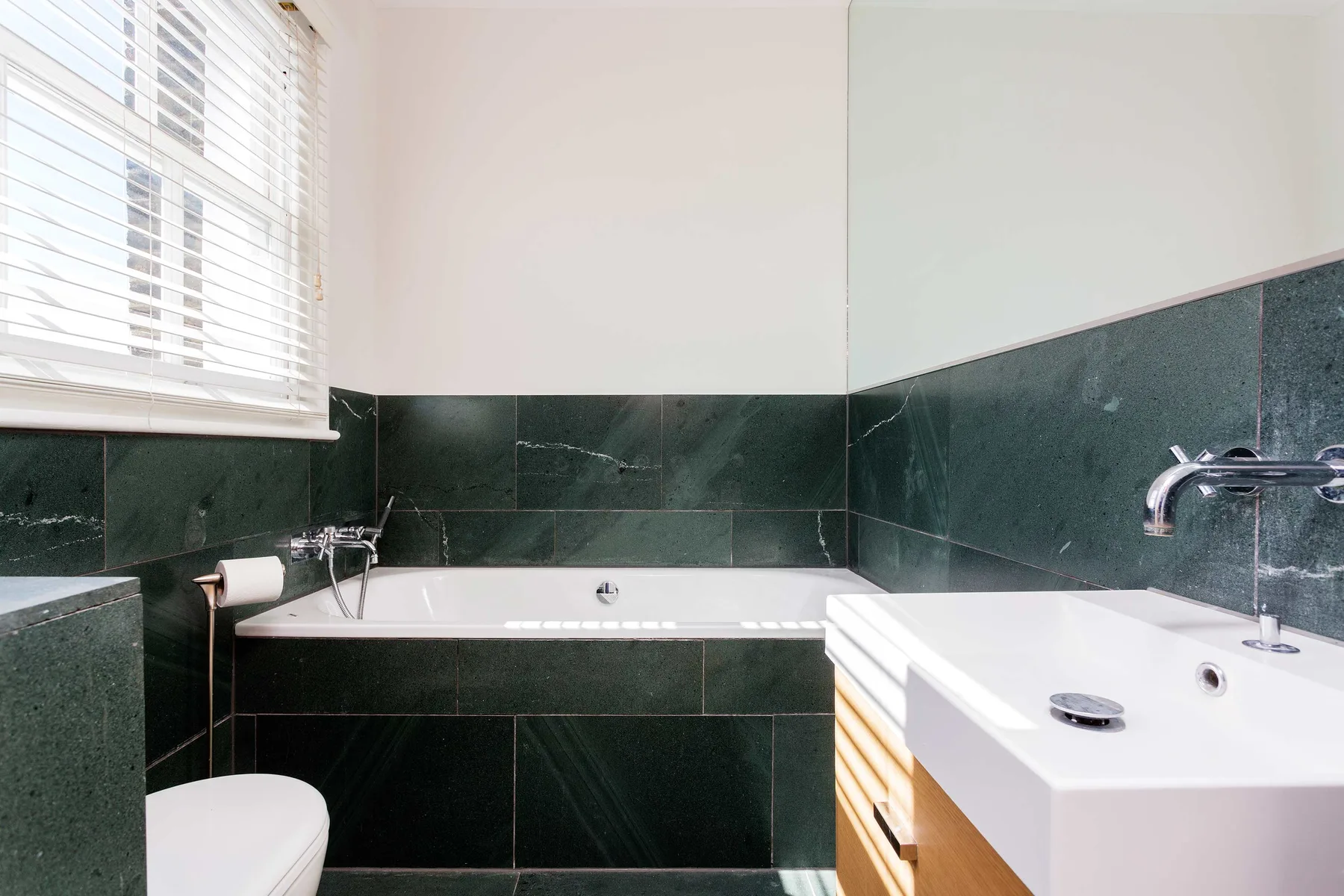 A bathroom with a bathtub, sink, and dark tiled walls.