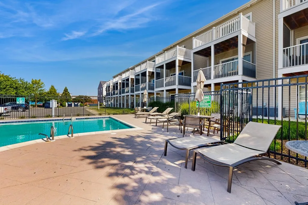 An outdoor pool patio with lounge seating beside a row of residential buildings.