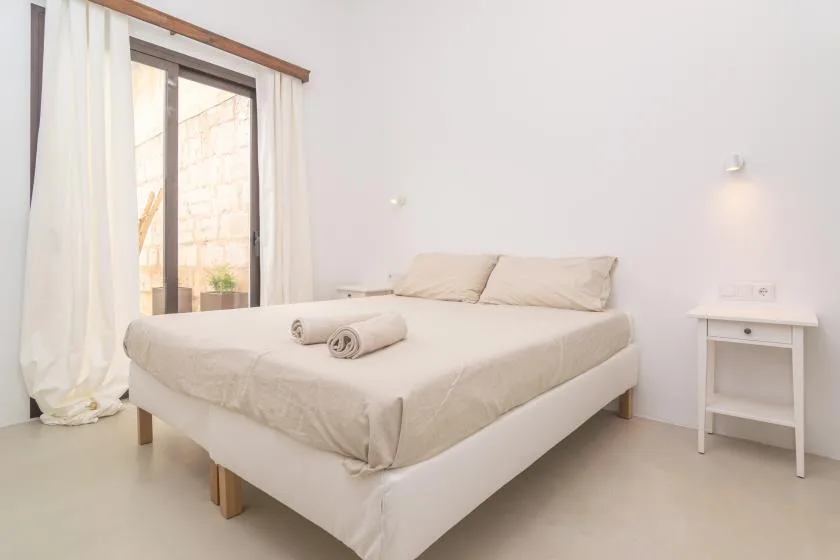 Un dormitorio luminoso con una cama bien tendida junto a una ventana grande.