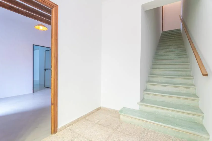 Un pasillo interior luminoso con una escalera y una puerta abierta.