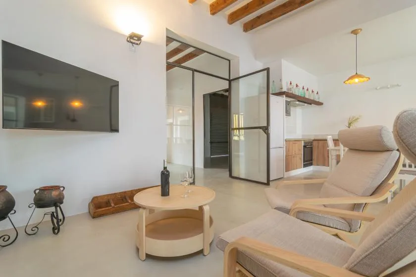 Una sala de estar luminosa con asientos, una mesa de centro y un televisor en la pared.