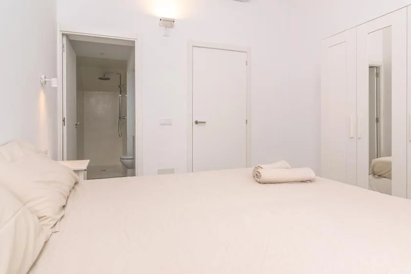 Un dormitorio luminoso con una cama bien tendida y una puerta al baño.