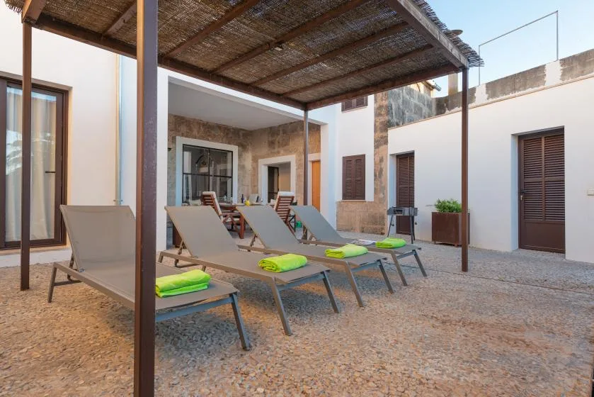 Una zona de estar en un patio bajo una pérgola de madera, con varias tumbonas.