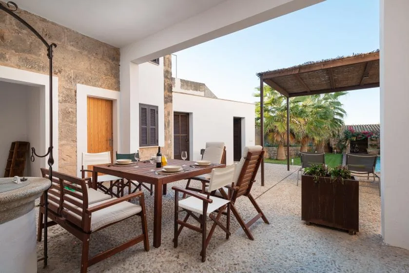 Una zona de comedor al aire libre con mesa de madera y asientos junto a un patio sombreado.